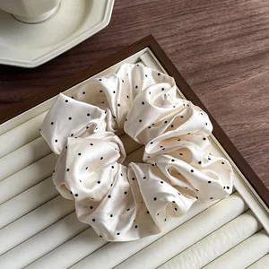 Close-up of cream satin scrunchie with black polka dots on an elegant display tray