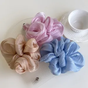 Three oversized pleated satin scrunchies in pink, champagne, and blue on a glass tray