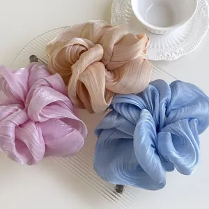 Detail of three oversized pleated hair scrunchies in pink, champagne and blue shimmering fabric
