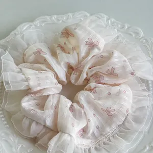 Detail eines cremefarbenen Organza-Haargummis mit rosa Schleife auf Perlen-Zierteller