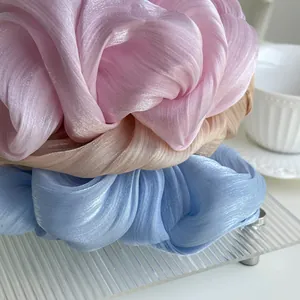 Three elegant pleated hair scrunchies in pink, beige, and blue with a glossy pearl finish