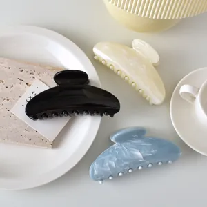 Three large marble-textured hair claws in black, cream, and blue on a minimal white tray