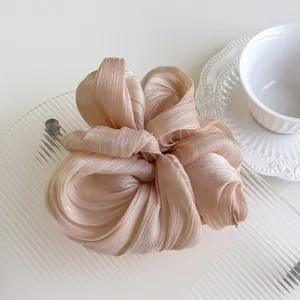 Macro detail of pleated champagne pearlescent fabric on a large scrunchie hair tie