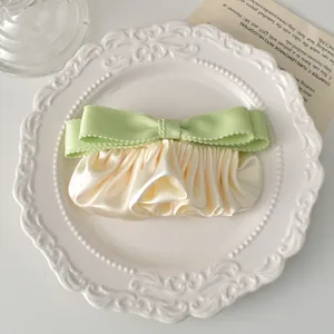 Vue détaillée de la barrette en satin crème avec ruban vert posée sur une assiette