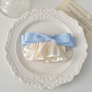 Détail de barrette nœud en satin bleu clair et ruban plissé crème sur assiette déco