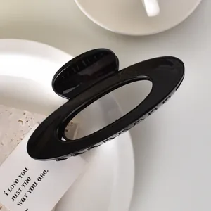 Macro shot of glossy black oval hollow hair claw clip on minimalist stone surface