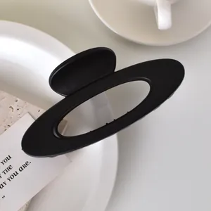Minimalist black hollow oval hair claw clip with matte finish on a white ceramic plate