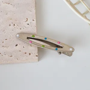 Close-up of silver metal hair clip featuring colorful enamel polka dots on stone surface
