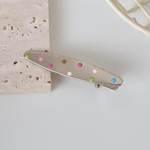 Macro detail of silver metal hair clip with vibrant multicolored polka dots on stone base