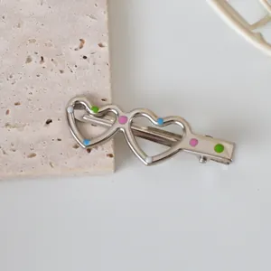 Close-up of silver metal heart hair clip with colorful dots on a stone surface