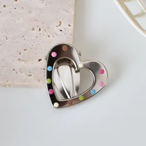 Detailed view of silver heart-shaped hair clip with colorful enamel dots on stone