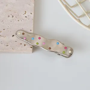 Detail of wavy metal hair clip with colorful polka dots on a minimalist stone background