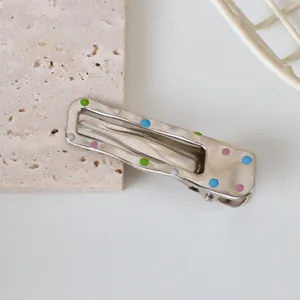Macro view of silver metal hair clip with colorful dots on beige stone background