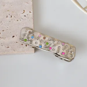 Close-up of a silver rectangular hair clip featuring colorful enamel dots on a stone base