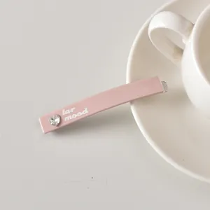 Détail d'une pince à cheveux rose avec strass en cœur et texte sur soucoupe en céramique