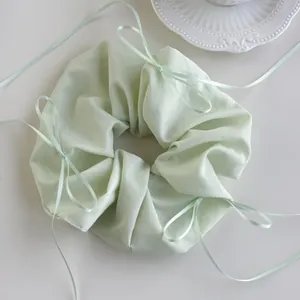 Detail of mint green scrunchie with delicate ribbon bows and satin fabric texture