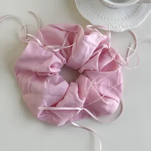 Detail of pink silk scrunchie with delicate ribbon bows on a clean white surface