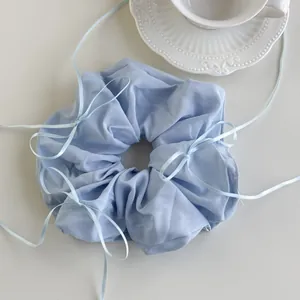 Macro shot of a light blue scrunchie with ribbons on a white background with a ceramic cup