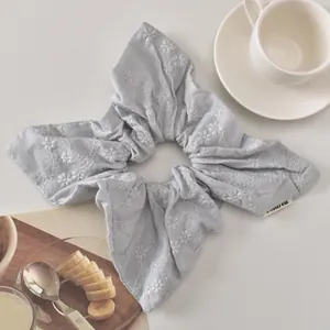 Macro shot of embroidered white floral patterns on a light blue cotton scrunchie