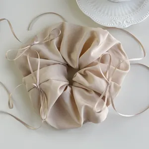 Macro detail of a beige satin oversized scrunchie with delicate silk ribbon bows