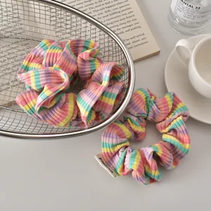 Close-up of rainbow striped ribbed scrunchies with fabric labels in a metal basket