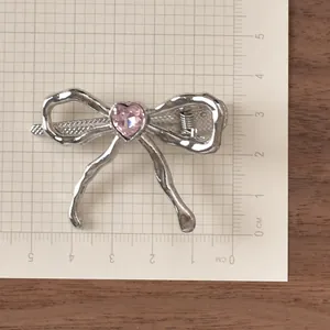 Detail view of 4cm silver bow hair clip with a pink heart gemstone on a scale grid