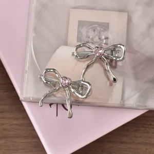 Macro detail of silver liquid metal bow hair clips with pink heart crystal accents