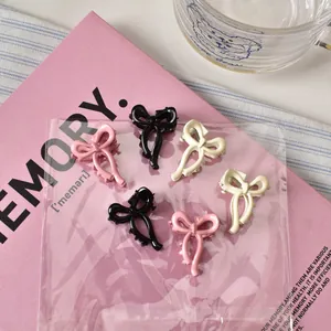 Dettaglio di 6 mini mollette per capelli a fiocco in nero, rosa e crema su scheda