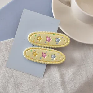 Détail de deux barrettes jaunes ovales avec étoiles 3D colorées sur carte bleue