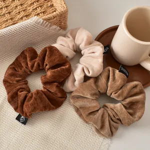 Close-up of three velvet oversized scrunchies in brown and beige on a cozy background