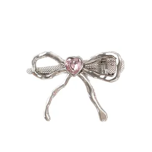 Silver bow hair clip with pink heart rhinestone and liquid metal texture on white base