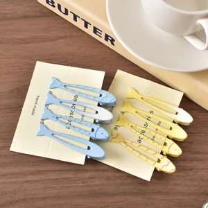 Fermagli per capelli a forma di pesce in metallo opaco blu e giallo su legno