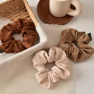 Close-up of velvet scrunchies in brown, camel, and beige with original woven labels