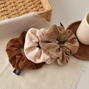 Detailed macro shot of three velvet scrunchies in coffee brown, cream and light tan colors