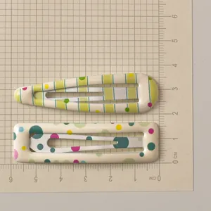 Detailed top view of two colorful polka dot metal hair clips on a scale ruler mat