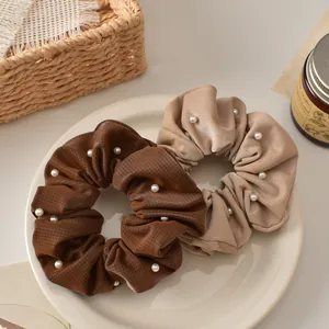 Brown and khaki textured fabric scrunchies with faux pearl accents in a ceramic tray