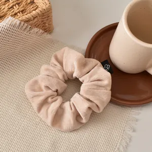 Detail of a large beige velvet scrunchie with fine texture and black flower logo tag