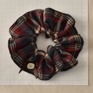 Detail of checkered plaid scrunchie with brown bow and button on a grid mat