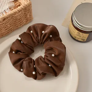 Detail view of coffee plaid hair scrunchie with white pearls on a beige ceramic plate