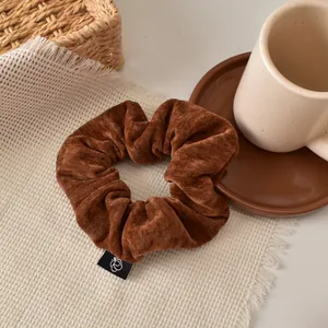 Detailed macro shot of brown velvet scrunchie texture with brand label and cafe props
