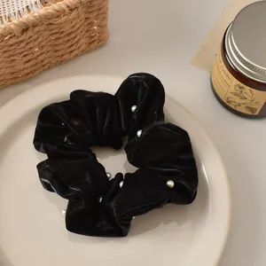 Detail view of a black checkered scrunchie with a white pearl on a beige ceramic plate