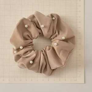 Detail of beige faux leather scrunchie with white pearls on a grid measuring mat
