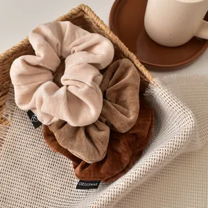 Brown velvet hair scrunchies set in beige and coffee tones on a white textured cloth