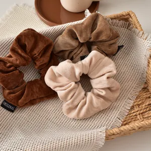 Three-piece set of velvet scrunchies in brown, caramel, and beige colors on a tray