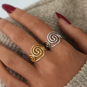 Close-up of golden and silver stainless steel swirl rings worn over a knit sweater