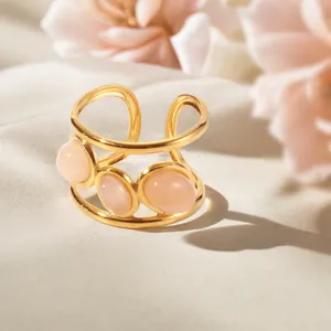 Gouden roestvrijstalen open ring met drie roze stenen op een zijden achtergrond