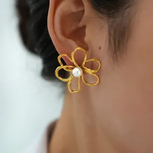 Orecchini a perno a fiore cavo dorati con perla mostrati sull'orecchio di donna