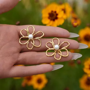 Dettaglio dell'orecchino a fiore traforato dorato con perla centrale tenuto in mano