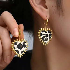 Detail of leopard print heart earrings with gold trim and textured finish worn by model