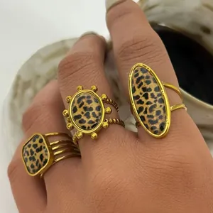 Close-up of three gold-plated geometric leopard print rings with textured bands on a hand